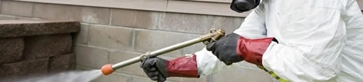 Pest control technician applying exterior insect treatment along a home foundation in Columbia, SC