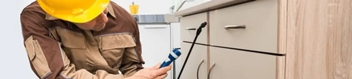 Roach exterminator applying treatment under kitchen cabinets in Columbia, SC