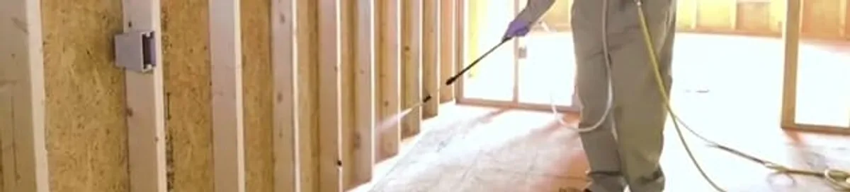 Termite treatment technician applying spray along framing and unfinished walls in Columbia, SC